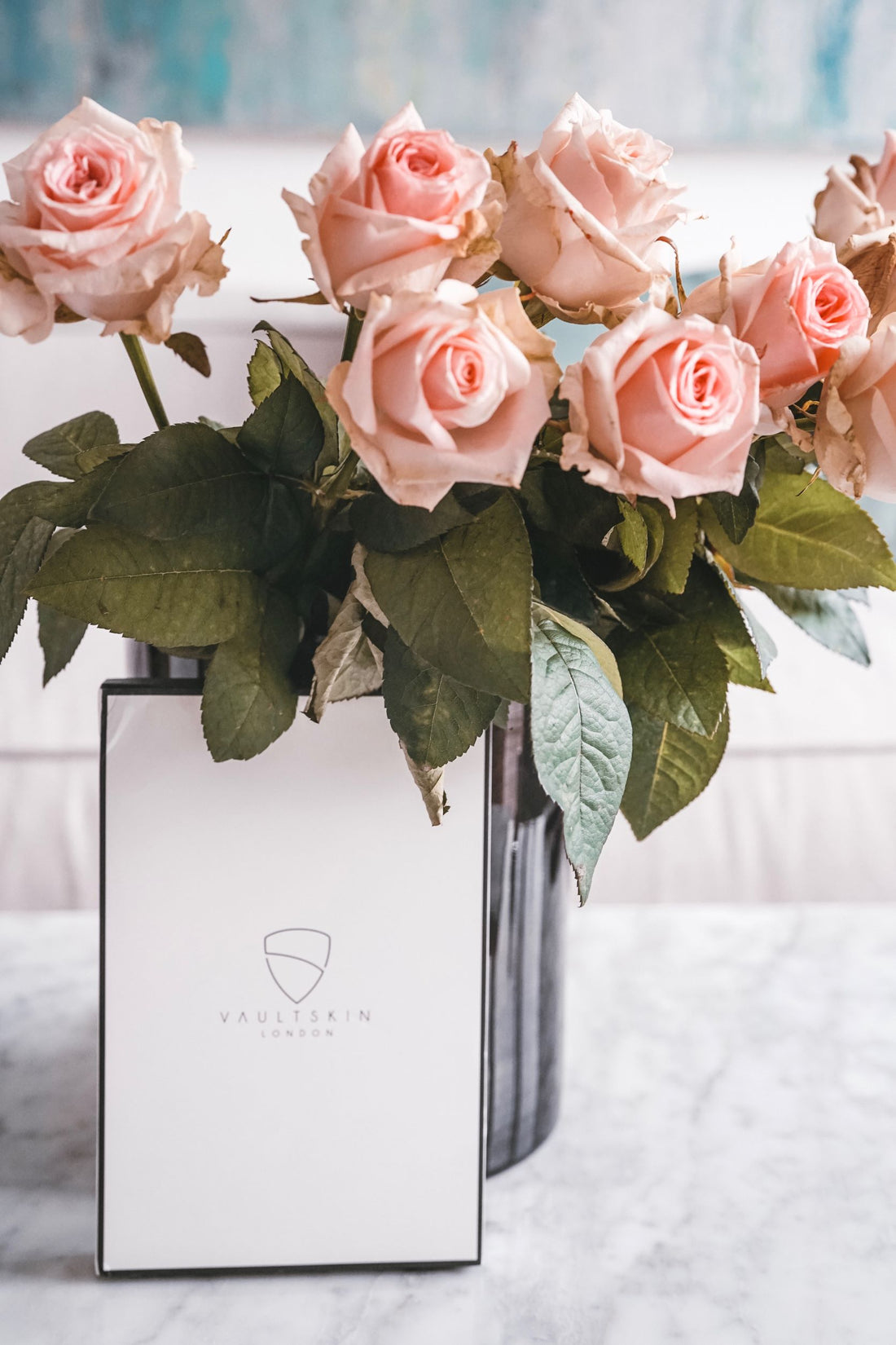 A white Vaultskin London box rests on marble beside a vase of pink roses