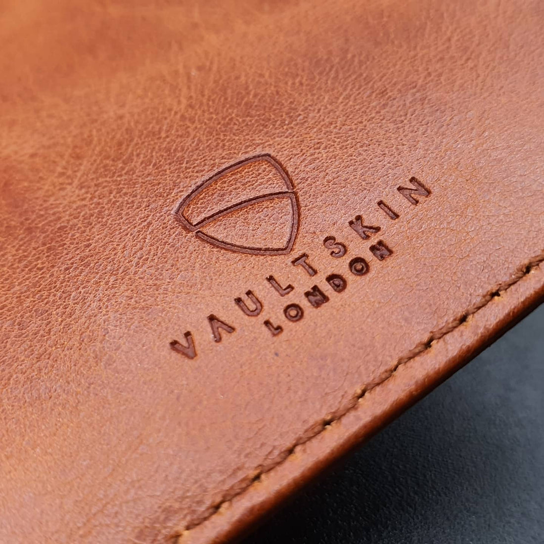 Close-up of the VAULTSKIN London logo debossed into tan leather beside a visible stitched edge