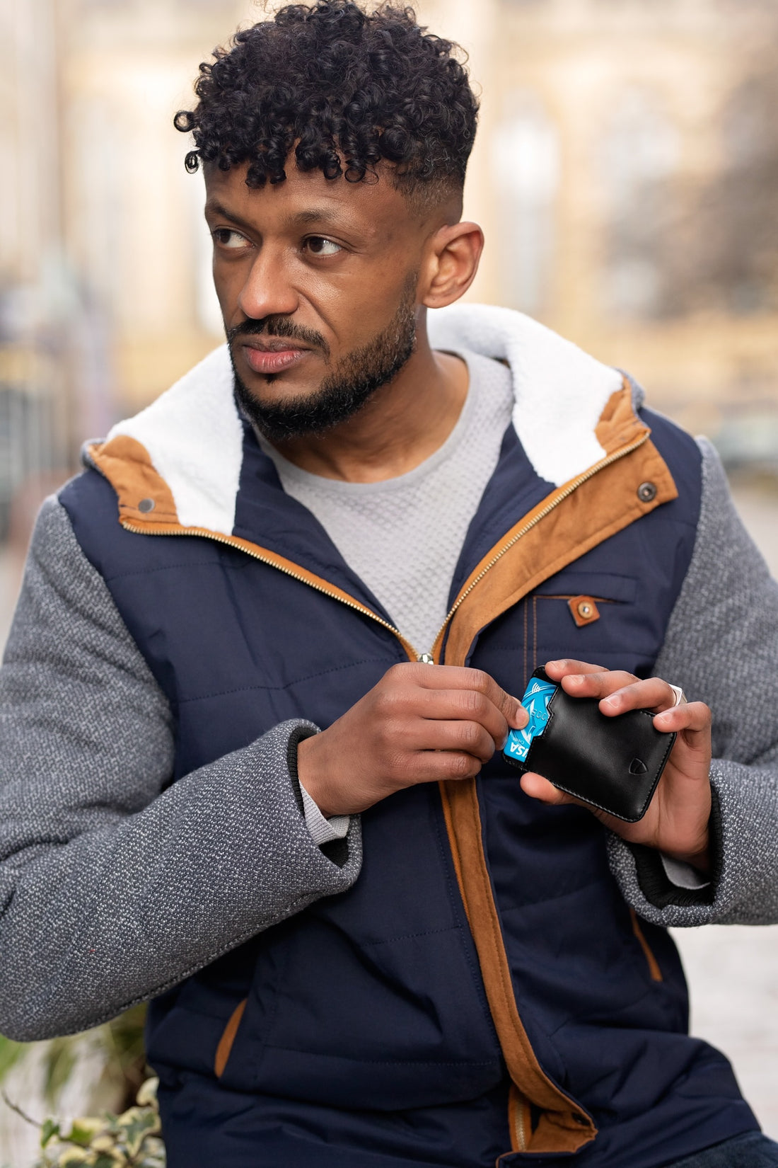 Man in a quilted vest pulls a card from the CHELSEA card holder while looking over his shoulder