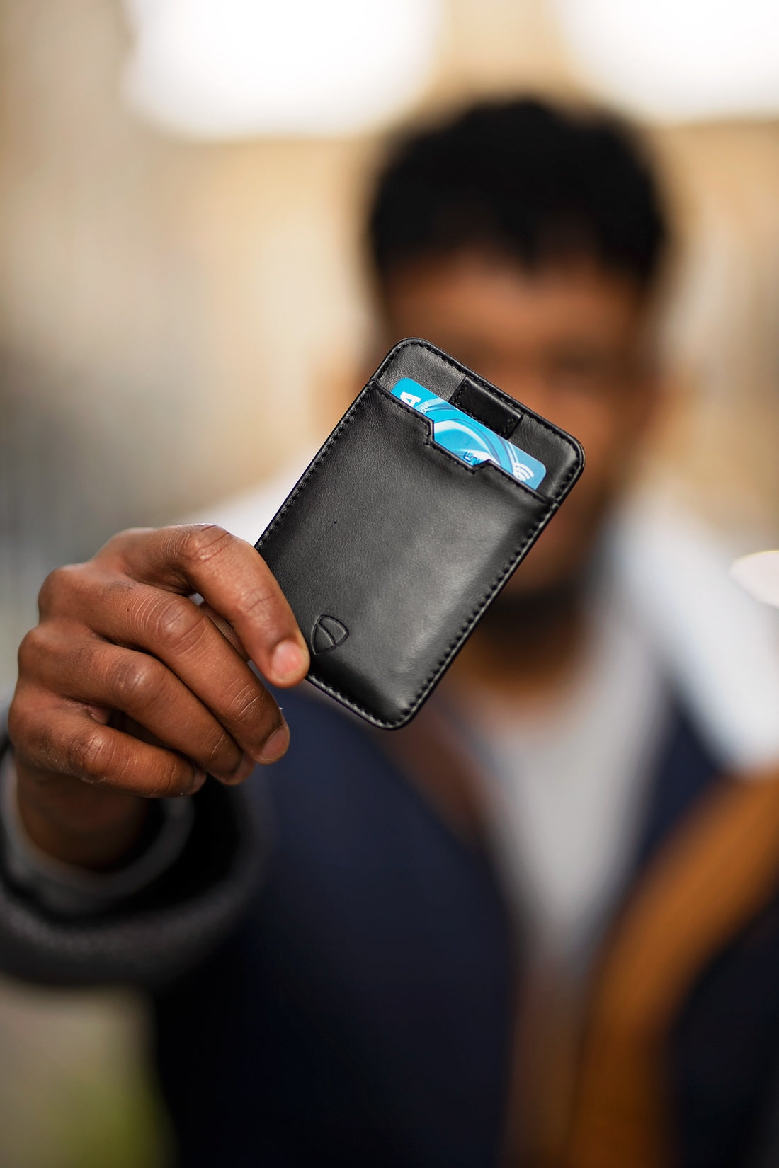 A hand holds a black leather card holder with a blue card tucked inside its slot
