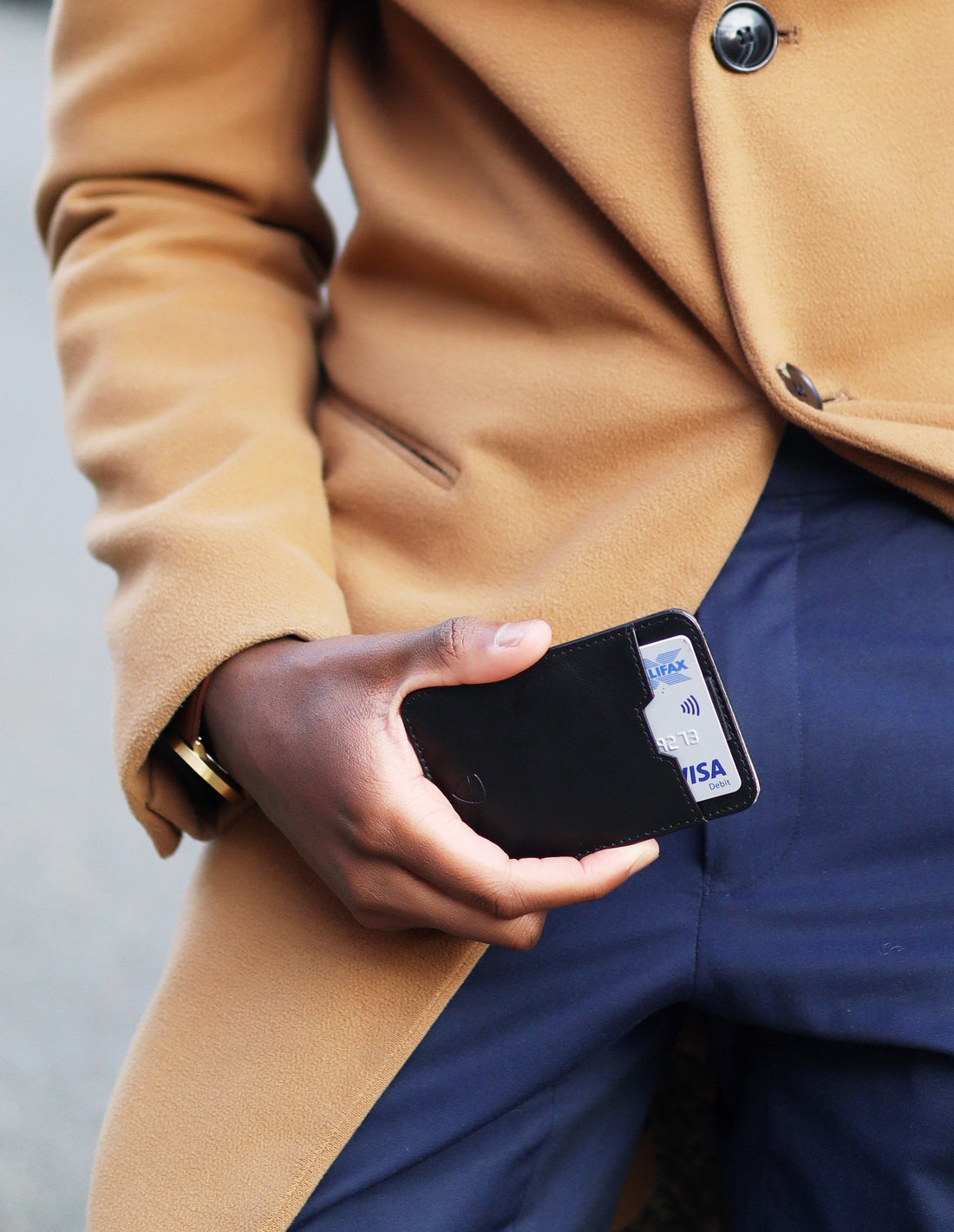 A hand holds a black CHELSEA RFID wallet with a debit card visible against navy trousers