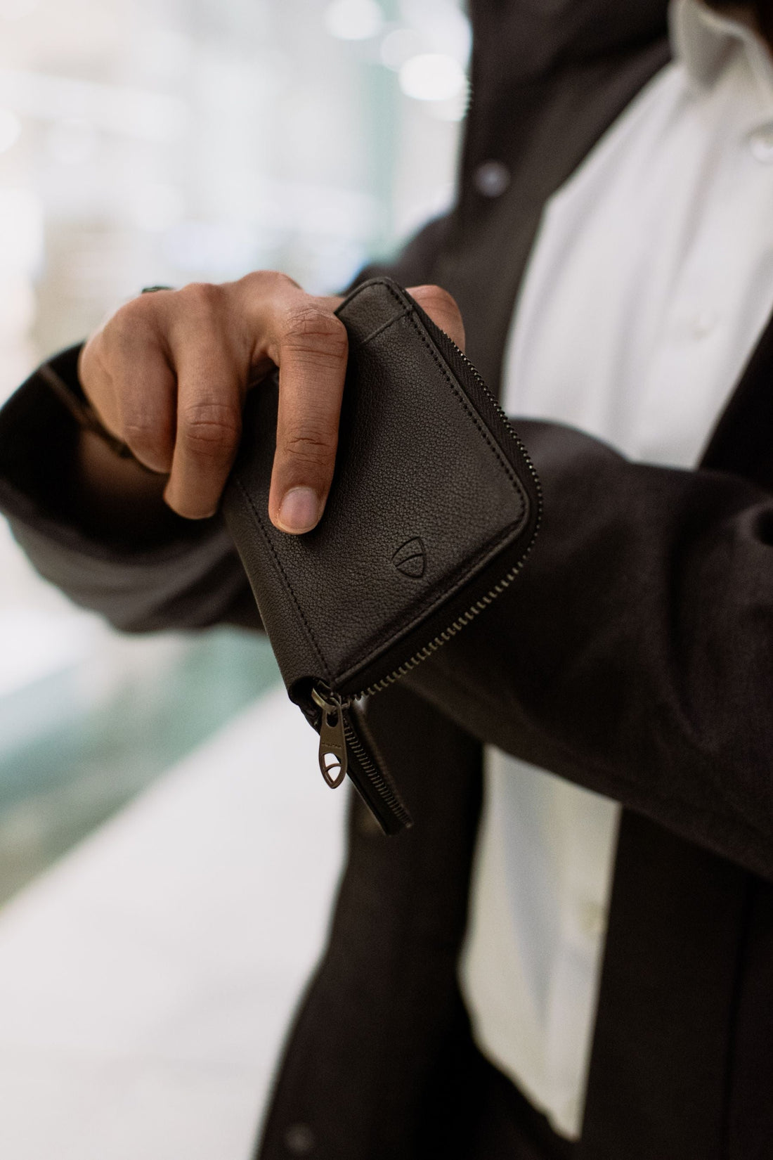 A hand holds a black leather zip-around wallet with a visible metal zipper and pull tab