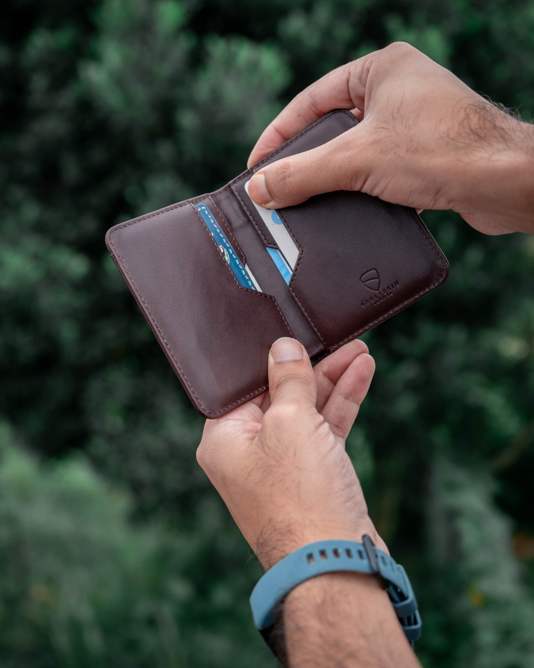 Two hands open a brown leather CITY bifold wallet to remove a card from its slot