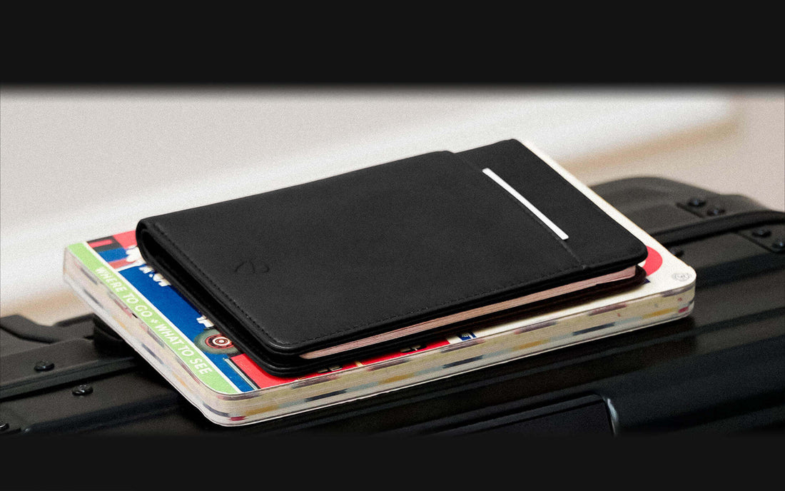 A black leather KENSINGTON passport holder rests closed on a travel magazine atop luggage