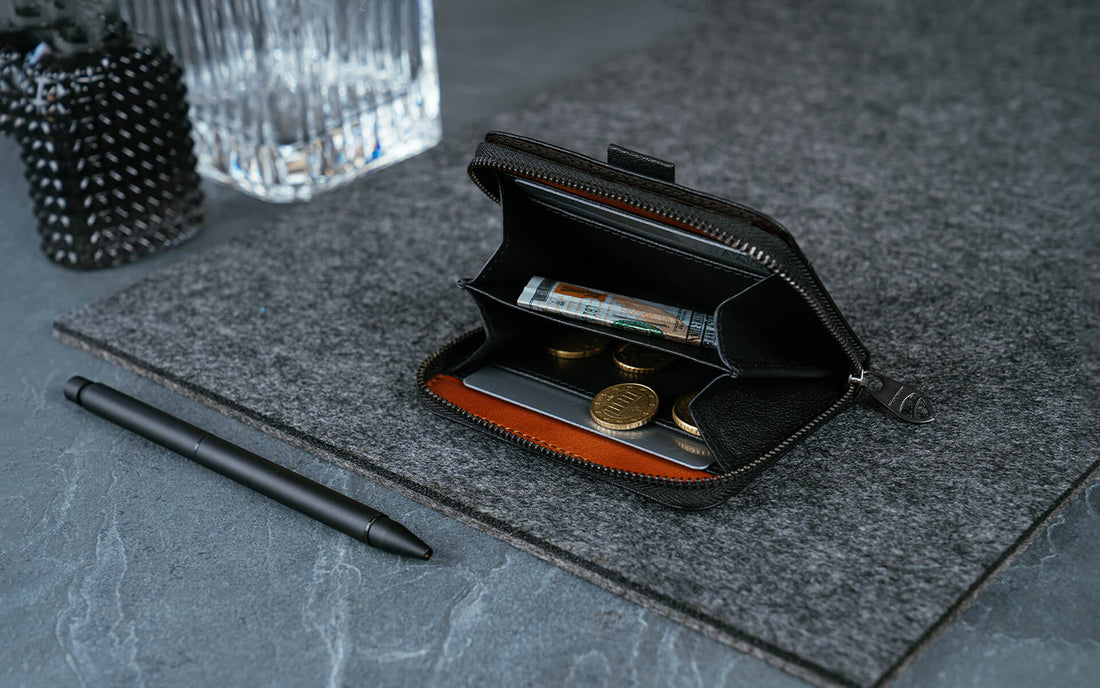 Open black MAYFAIR zip wallet showing a folded banknote, 1 card and 4 coins beside a pen