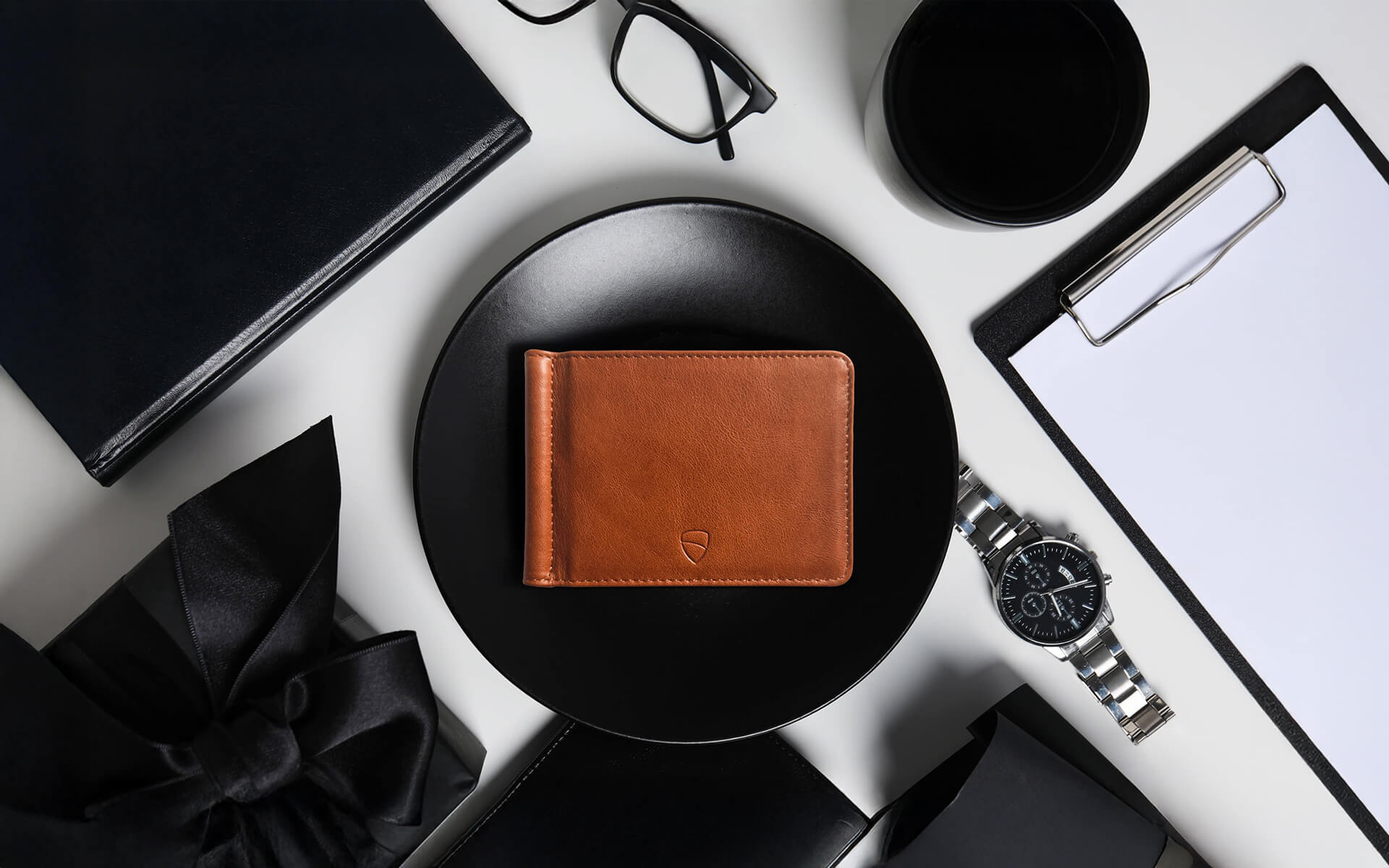 Vaultskin BROMPTON cognac leather wallet on black desk with watch and notebook, luxury slim RFID wallet for men and women
