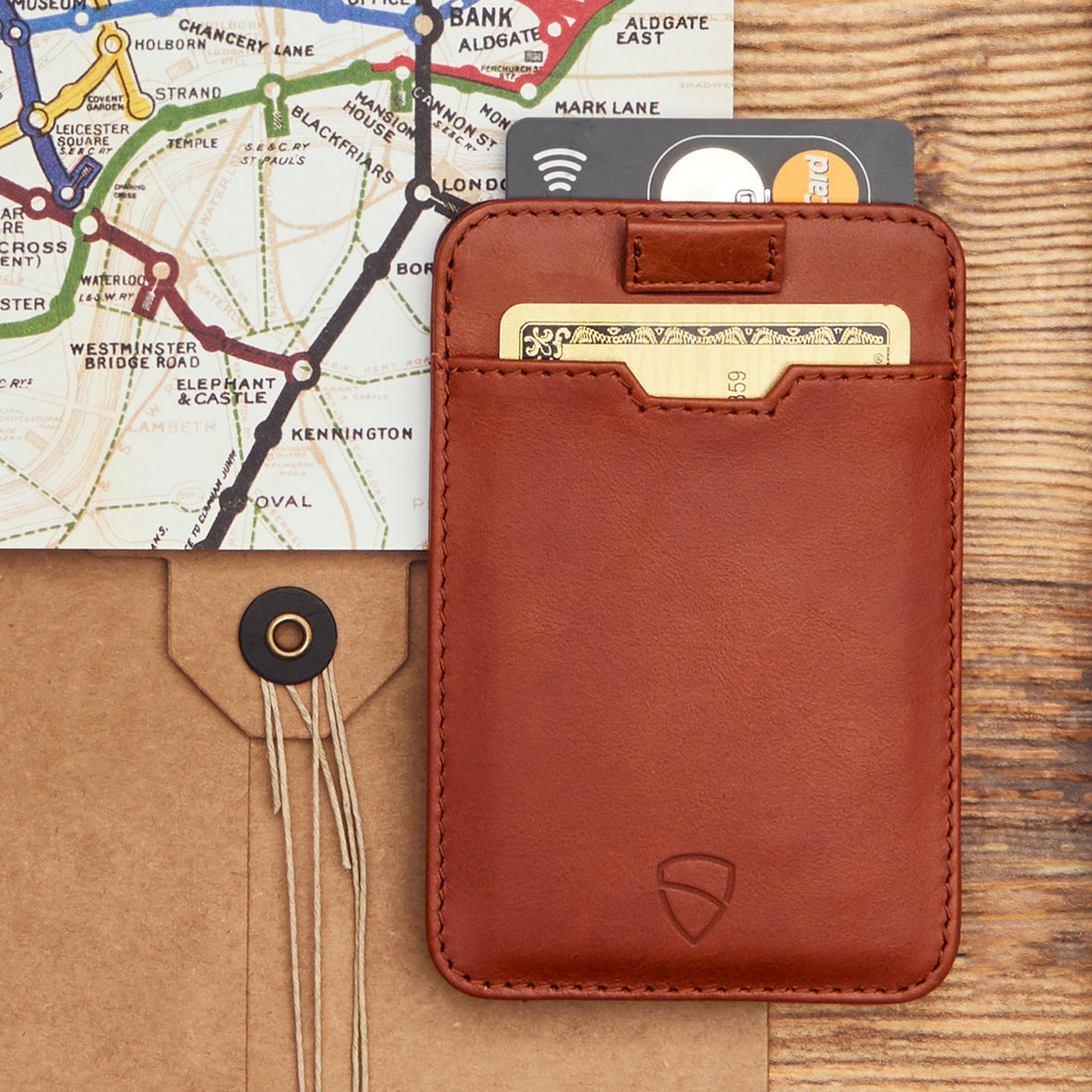 VAULTSKIN Chelsea minimalist RFID protected leather wallet in cognac lies in front of a map and envelope