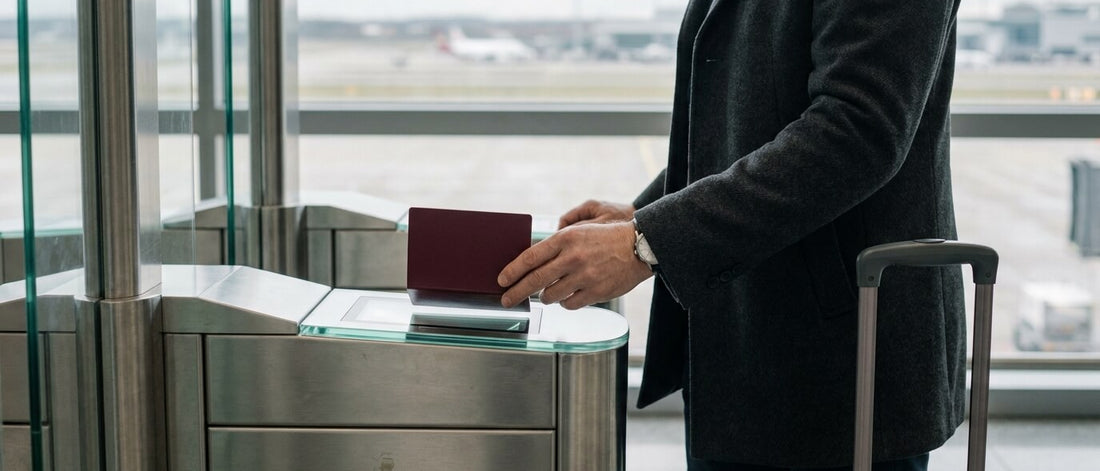 A traveller holds an open passport over the scanner of an automated airport passport gate, his suitcase at his side