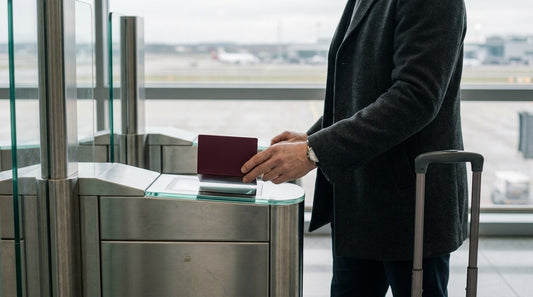 A traveller holds an open passport over the scanner of an automated airport passport gate, his suitcase at his side