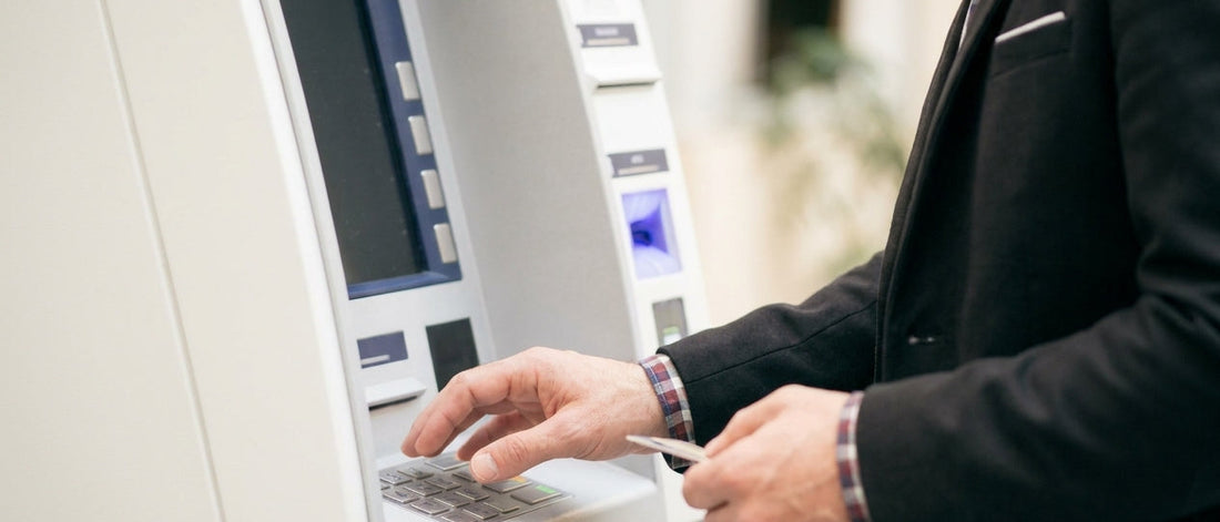 Man in a suit using an ATM while holding a bank card, illustrating contactless card security