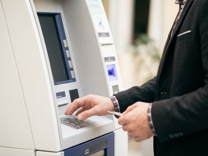 Man in a suit using an ATM while holding a bank card, illustrating contactless card security