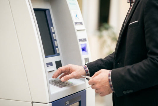 Man in a suit using an ATM while holding a bank card, illustrating contactless card security