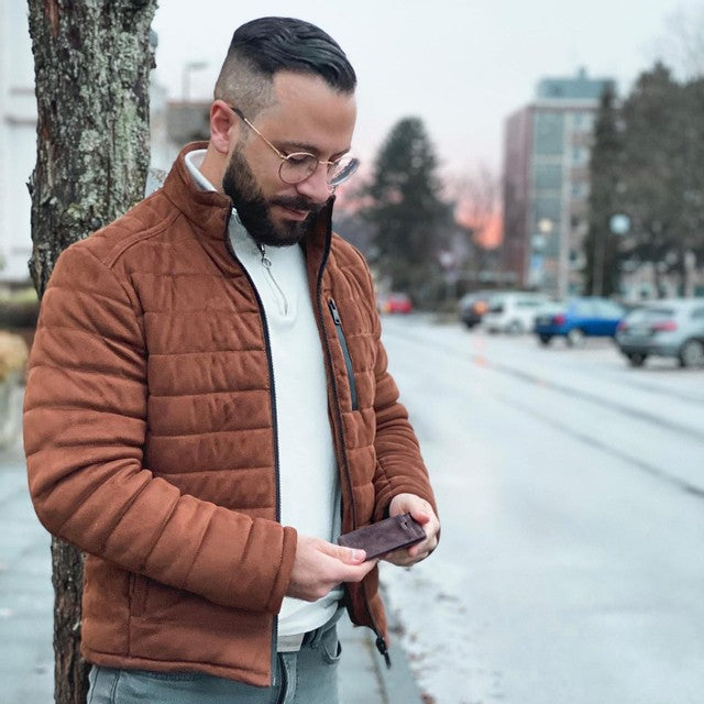 Man standing on a street looking down at a wallet in his hands.